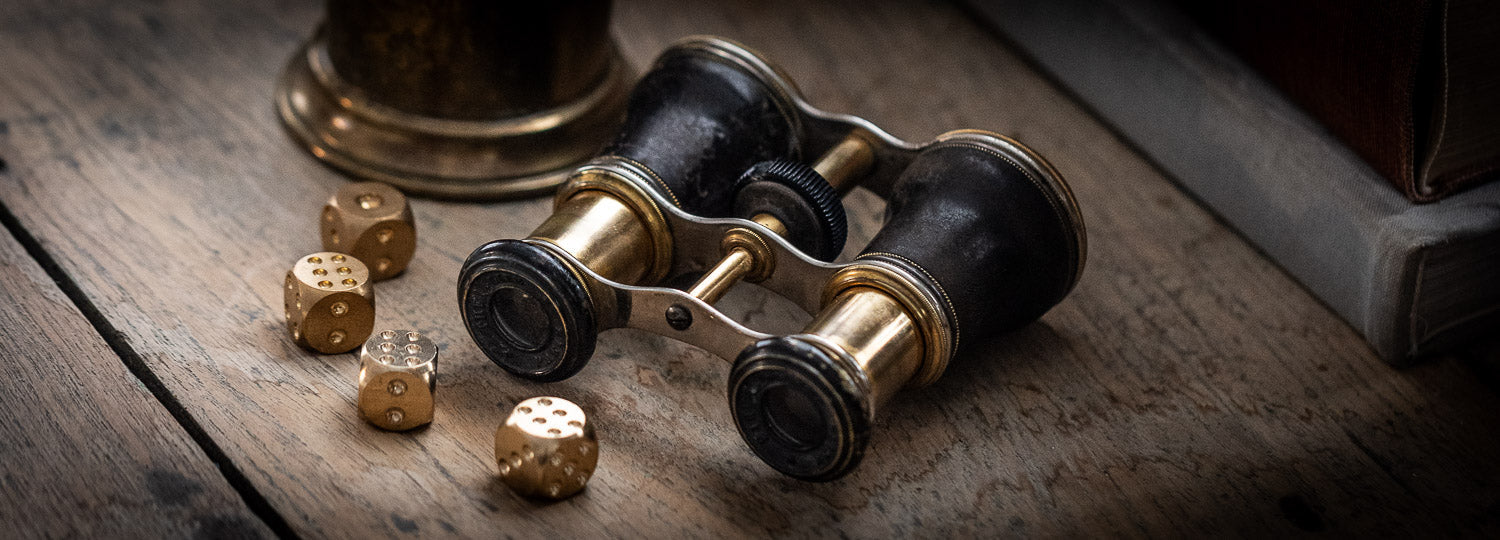Brass and leather opera glasses next to brass dice