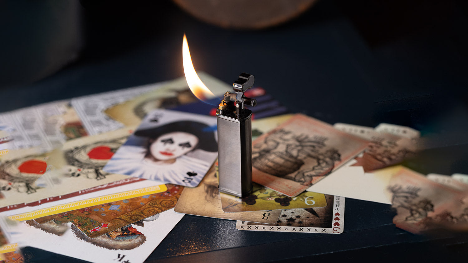 A black Kiribi Kenshi lighter with flame lit standing over a pile of decorative playing cards