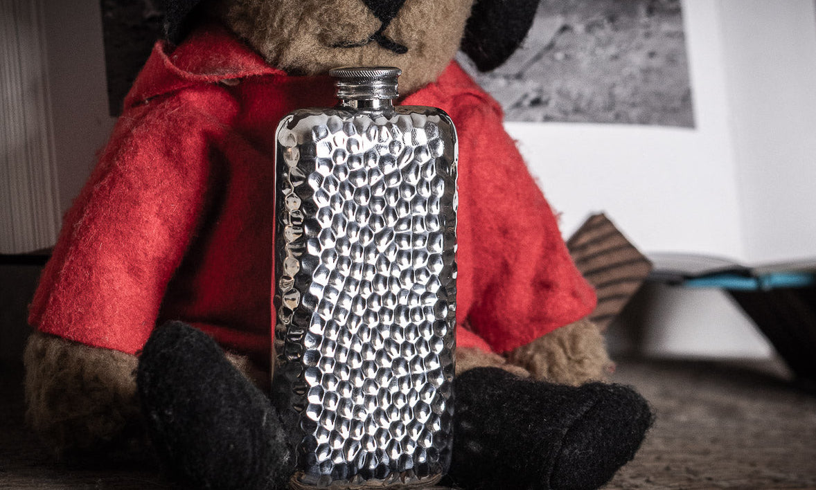 hammered pewter flask next to a Paddington bear