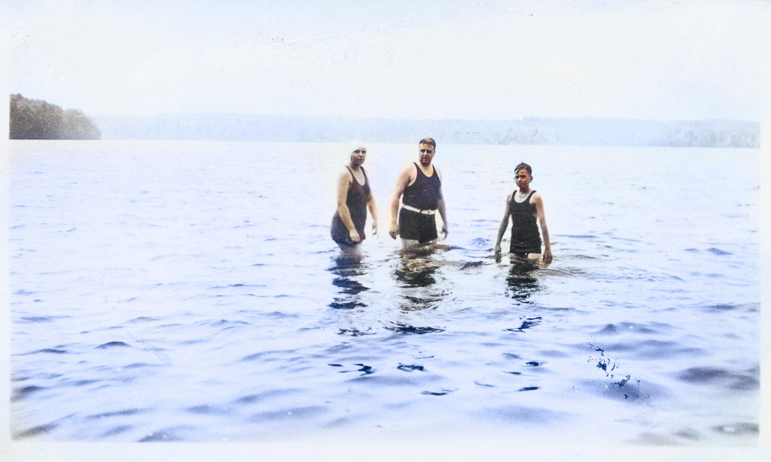 Three people standing in the water with a clear sky background